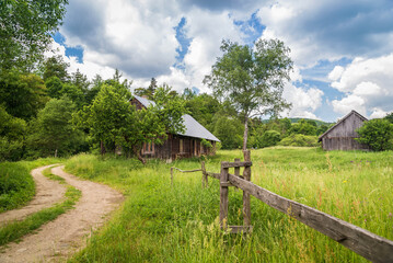 Polna droga, stara chata, drewniany płot, zielona łąka z drzewem pod błękitnym niebem w słoneczny dzień (Beskid Niski)