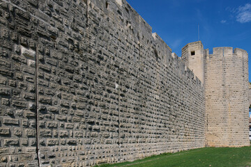 Mury obronne i starożytne miasto, ciasne uliczki, stłoczone domy, czerwone dachy, zielona roślinność na ulicach.