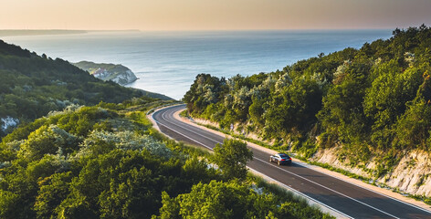 Driving on a coast road. Aerial view of a car driven on an amazing curved waving road at the Sea shore in Balchik sea resort in Bulgaria.