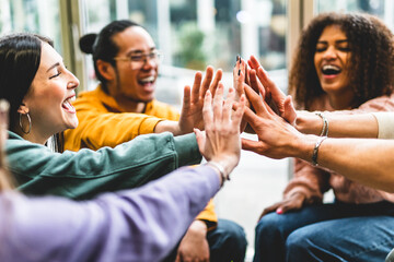 Multiracial happy young people stacking hands-Group of diverse friends having fun unity together indoors at table of community-Human resources Concept Creative and Relationship Youth Culture 