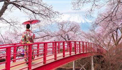 Woman traveller with a red umbrella and walking over the bridge with Fuji mountain and Sakura flower background