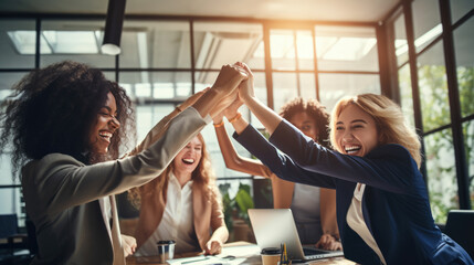 Moment of celebration, with a group of women in a business setting giving each other a high five, all smiling and exuding happiness and a sense of achievement.