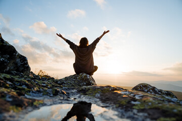 Girl meets morning sunrise in the mountains sitting on a stone, mountain landscape, meditation in nature, happy man.