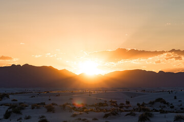 Sun rays peeking over the mountains and dunes of White Sands National Park, New Mexico during sunset