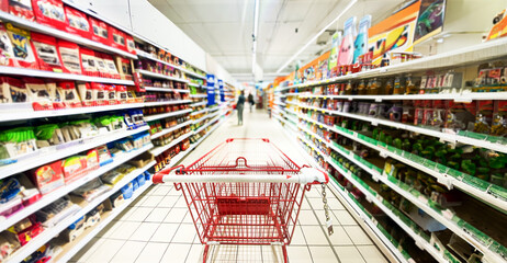 Pusty koszyk, wózek sklepowy w supermarkecie, rozmazane tło, wnętrze sklepu, supermarketu, wózek na zakupy, półki sklepowe z produktami. Hipermarket. Baner, miejsce na tekst.