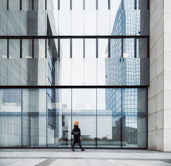 A female leader walks in front of an office building in cloudy weather. She meets a male businessman. They are discussing a new deal. They are dressed in business clothes.