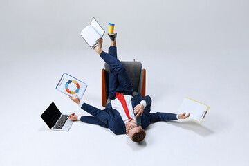 Businessman lying on ground, his lags in multiple directions, managing papers, laptop, and phone calls. Chaos meets productivity. Concept of business, work overload, multitasking, corporate stress