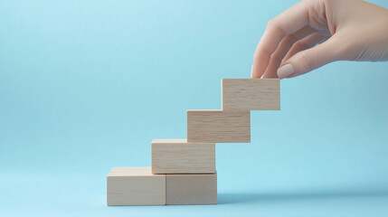 Na jasnoniebieskim tle kobieta skupia się na układaniu drewnianych klocków, które tworzą schody symbolizujące rozwój w biznesie.