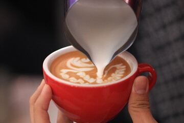 Milk pours into cup creating coffee art by barista.