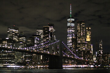 Nocny widok na Brooklyn Bridge i panoramę Manhattanu z DUMBO. Oświetlony most, refleksy w wodzie i tętniące życiem miasto tworzą niezapomniany klimat Nowego Jorku.