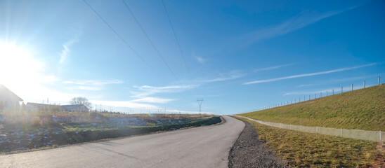 Kręta asfaltowa droga przez wzgórza na terenach wiejskich w województwie świętokrzyskim. Asfaltowa droga łagodnie wije się przez pagórki pod czystym, błękitnym niebem. Droga jest otoczona polami.