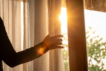 woman's hand She opened the curtains on the window. There was morning light through the window in her room, looking at the view of the mountains and trees as the sun rose 