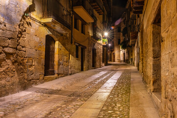 Alley with medieval stone houses at night lit with street lamps, Valderrobles, Teruel.