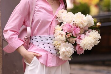 Stylish woman with beautiful peonies on city street, closeup