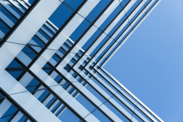 Photo shows the exterior of a modern glass office building with reflective windows. The image is taken from a low angle, emphasizing architectural lines and urban design.