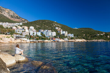 Woman looking at sea and historical town Kash placed on hills by coast of mediterranean sea in Antalya region in Turkey. Capturing summer vacation, popular place for family travel with kids.