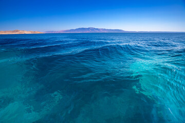 Morski pejzaż z kamienistą linią brzegową i odległymi górami pod czystym niebieskim niebem, Grecja, greckie wyspy