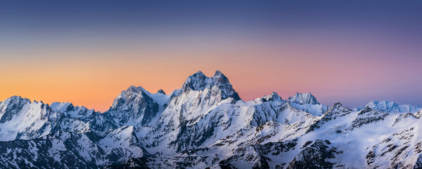 Panoramic view of the Ushba and Skhelda peaks at sunrise under the clolrful sky. Steep rocky caucasian mountains, a part of the Main Caucasian range, in winter sunny morning.