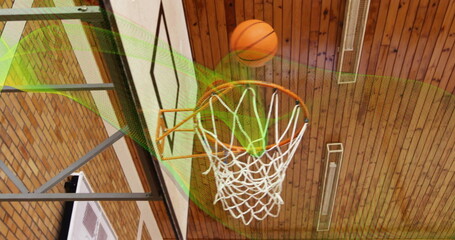 Passing orange basketball through metal rim and net inside gymnasium with backboard, lights