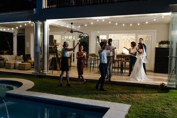 Celebrating joyfully, guests at outdoor wedding reception near pool with string lights