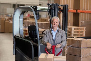 Manual pallet jack carrying stacked cardboard boxes past parked forklift under bright lights