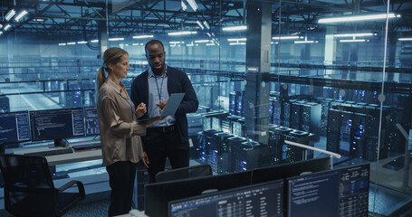 Male Cloud Architect and Female Database Engineer Review Data Storage Protocols on a Shared Laptop in a Data Center. Team Strategizing Ways to Improve Service for Enterprise Clients