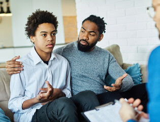 Father with his teenage son at meeting with social worker, psychologist discussing mental health family sitting on sofa in psychotherapist office