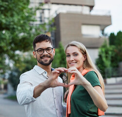 Portrait of a happy young couple standing in front of their new house, with keys in hands, smiling man and woman posing near modern home, making selfie, real estate agency, house owners, young family