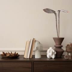 Interior design of aesthetic living room interior with copy space, wooden sideboard, vase with dried flowers, books, modern sculpture, beige wall with stucco and personal accessories. 