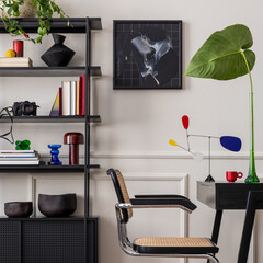 Workplace interior with mock up poster frame, black desk, rattan chair, stylish rack, books, yellow vase with leaves, modern sculpture, wall with stucco and personal accessories. Home decor. Template.
