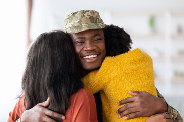 A soldier in military uniform is warmly embraced by two family members. The joyful atmosphere captures love and happiness as they reunite in a welcoming living room.