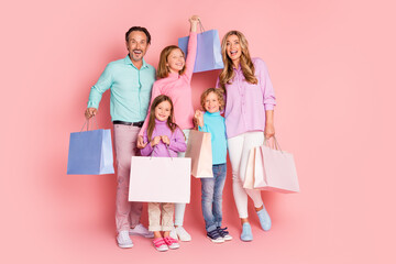 Happy family shopping day with parents and children posing with colorful bags against a pink background