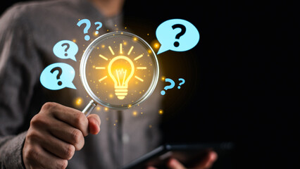 Businessman holding magnifying glass with glowing light bulb and question marks, representing problem solving, finding solutions, critical thinking, and innovative decision making.