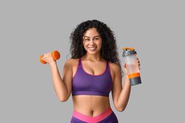 Sporty young African-American female coach with dumbbell and water bottle on white background