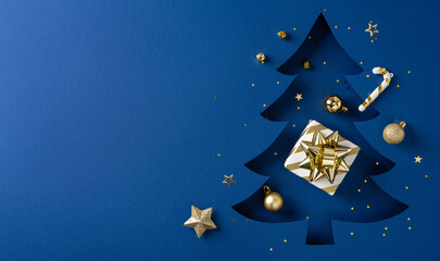 A blue backdrop hosts a dark blue Christmas tree cutout, gold gift box with bow, ornaments, and scattered stars creating a joyful holiday mood for Christmas and New Year visuals