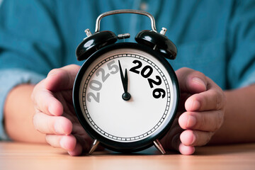 Businessman holding an alarm clock showing the transition from 2025 to 2026 symbolizing time change new year planning future goals strategy and preparation for business and personal development