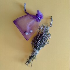 bolsita morada de regalo para joyas con dos pendientes de perla dentro y al lado ramito de flores moradas silvestres