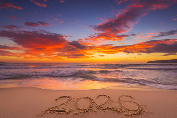 Happy New Year 2026 tropical island, beautiful sunrise over the beach and sea horizon with text 2026 handwritten in the sand