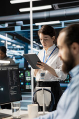Engineer using tablet in data center to deploy server virtualization updates, configuring equipment using software tools. IT worker reviewing hardware analytics, ensuring reliable network operations
