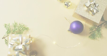 Styling flatlay with matte purple bauble on beige tabletop, wrapped gifts, fairy lights, copy space