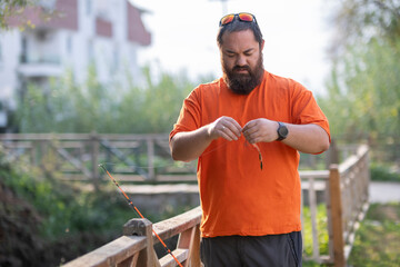City life meets nature: man fishing in stream. Man fishing with rod in urban stream.Urban fishing scene with angler by city creek. Angler preparing and fishing in urban waterway.