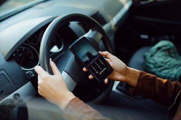 Close-up of a female driver using her smartphone behind the wheel.