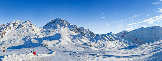 panorama on ski resort in tarentaise valley, savoie with snowy mountain range and ski slope under blue sky