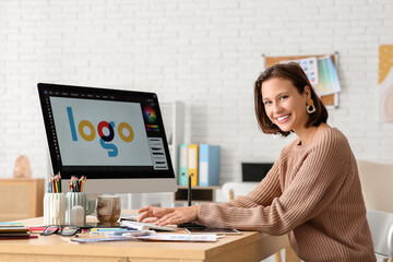 Young female designer working with graphics tablet and computer at table in office