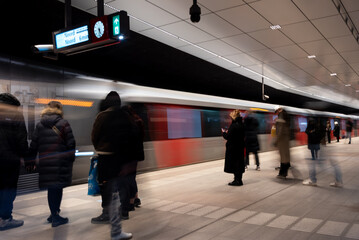 Commuters waiting on metro platform with motion blur. Rush hour metro station. Train moving. 
