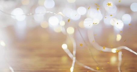 Twinkling thin silver wire fairy lights reflecting on warm wooden tabletop, with gold star confetti