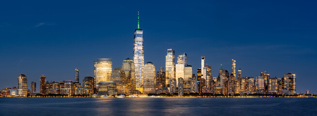 Panoramic view of New York City Lower Manhattan skyline at dusk with the Hudson River. Illuminated skyscrapers of the Financial District and World Trade Center