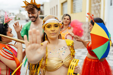 Woman raising her hand in a stop gesture to reject harassment during a Brazilian carnival street celebration, while friends support her around.