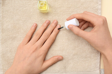 Female hands applying cuticle oil with brush on beige towel