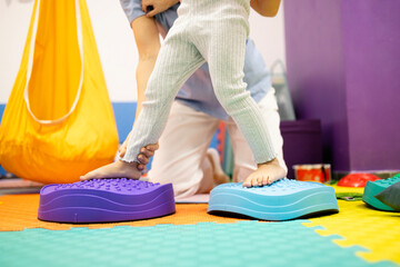 Pediatric physiatrist supporting a child balancing on sensory stepping stones during a physical therapy session for rehabilitation and developmental coordination